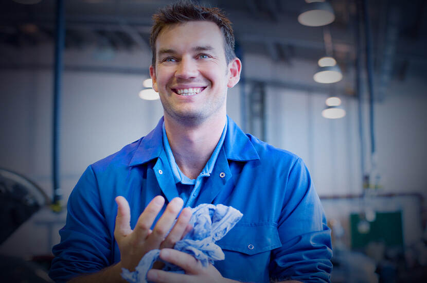 Man met blauwe overall kijkt lachend de camera in terwijl hij zijn handen afveegt met een doek