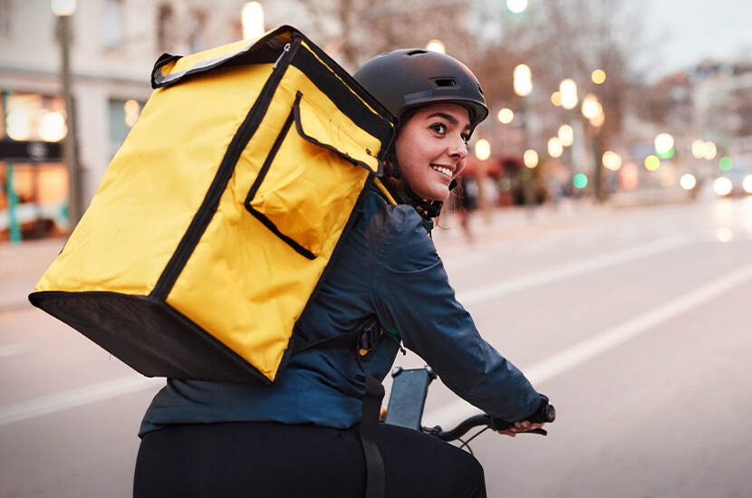Meisje met een grote gele tas op haar rug fiets door een straat